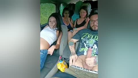 A video shows a young Asian woman with long black hair in a tight white crop top, sitting next to a muscular tattooed man in a graphic T-shirt, both in a car.