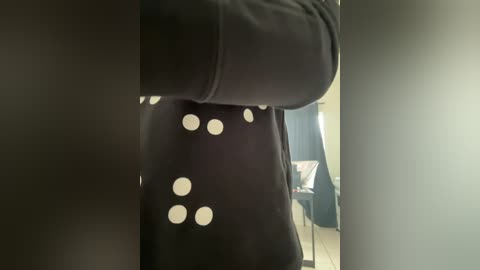 A video showing a person in a black, round-backed chair with white polka dot upholstery, situated in a dimly lit room with a window allowing light to enter. The background reveals a blurred desk and a chair, adding a casual, homey ambiance.