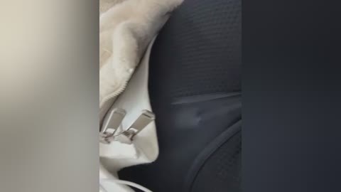 Video of a close-up of a person's upper thigh and hip, wearing black leggings and a beige jacket with a white zipper, blurred background.