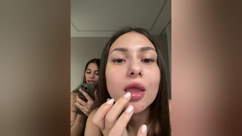 A close-up video of a young woman with light brown skin and straight, dark hair, wearing a nose ring. She is in a bedroom, taking a selfie with a smartphone.