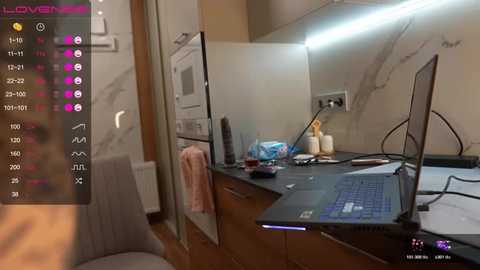 Video of a tidy, modern kitchen with a black laptop on a wooden counter, surrounded by a microwave, a water bottle, and a white towel.