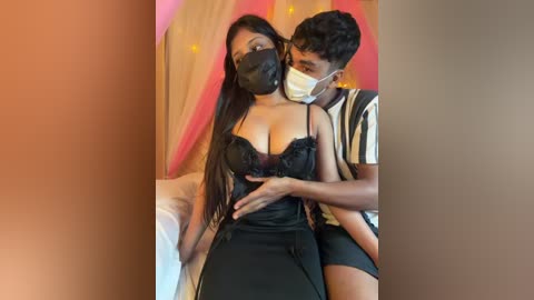 Video: A Black woman with long hair, wearing a black lace bra, black face mask, and black skirt, being held by a young Black man in a striped shirt.