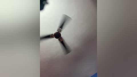 Video of a ceiling fan with three blades, spinning in a white room, blurred edges, slightly out of focus.