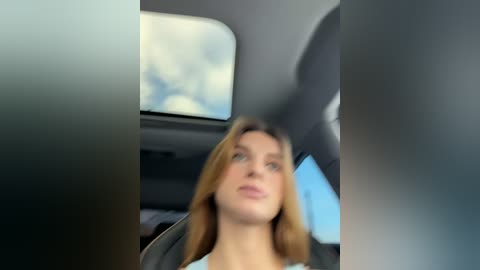 Video of a blonde woman in a car, wearing a blue top, with a clear blue sky visible through the window, driving in a modern vehicle.