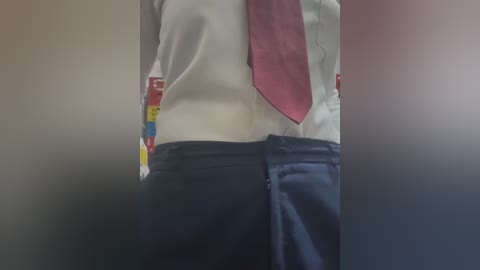 Video of a person wearing a white shirt with a red tie and navy blue pants, blurred background with red and yellow horizontal stripes.