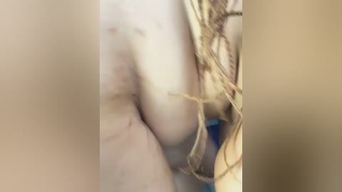 Video of a nude, fair-skinned woman with long, blonde hair, partially obscured by a rope, with her breasts visible. The background is blurred, creating a focus on her body and the rope.