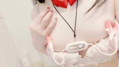 Video of a pale-skinned woman in a white lace bra, wearing a red bow tie, and holding a white breast pump.