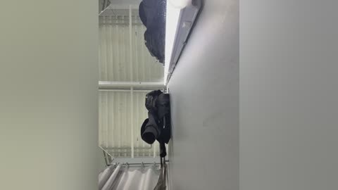 Video of a black camera attached to a white wall in a dimly lit room with a corrugated metal ceiling. The camera's lens is pointed upwards.