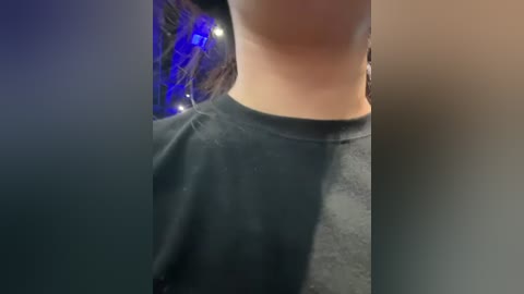 A video showing a person's torso in a dark grey shirt, with a tattoo on their side, partially obscured by the shirt. The background features a blurred, blue-lit area, suggesting an indoor setting with ambient lighting.