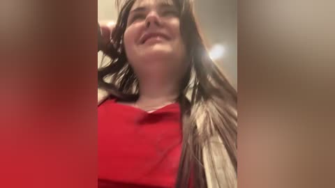 A video shows a woman with long brown hair, fair skin, and a red top, smiling widely with her eyes closed, against a blurred background.