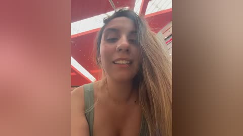 Video of a smiling young woman with long, straight brown hair, wearing a green tank top, inside a brightly lit, red and white retro diner with a geometric ceiling pattern.