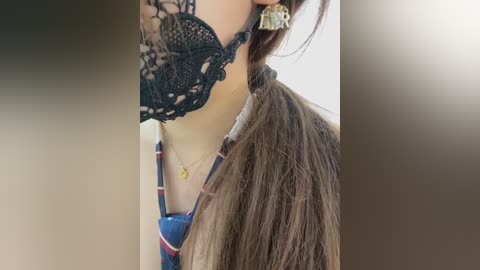 Video of a woman with long, straight brown hair, wearing a black lace bra and a plaid shirt. She has gold hoop earrings and a colorful beaded necklace. The background is blurred.