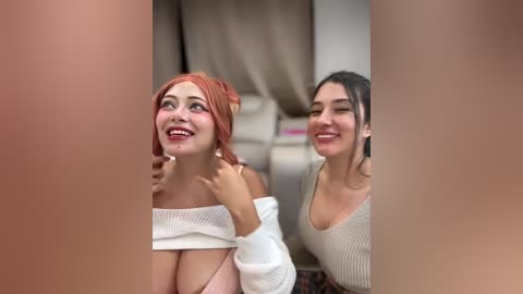 Video of two smiling women, one with a red headscarf, the other in a beige top, sitting on a beige couch. The background features a beige curtain.