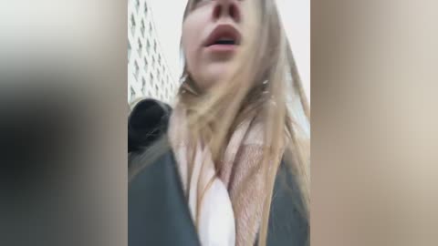 Video of a close-up of a woman's face with long, blonde hair, wearing a white shirt and gray jacket, mouth slightly open, blurred background.