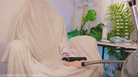 Video of a person receiving a facial massage with a white towel covering their face. A green plant and skincare products on a shelf are visible in the background.