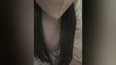 Video of a woman's face and chest, with long, straight black hair and a light-colored shirt, lying on a pillow. The image is dimly lit, creating a moody atmosphere.