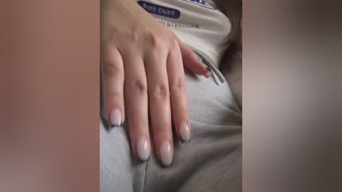 Video of a light-skinned hand with neatly manicured nails resting on a gray shirt. The background is blurred, focusing attention on the hand and shirt.