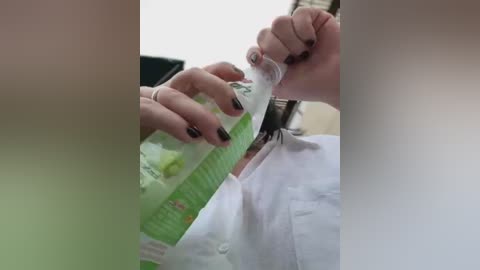 Video showing a person with fair skin, black nails, and a white shirt pouring water from a green bottle with a white cap into their mouth. The background is blurred.