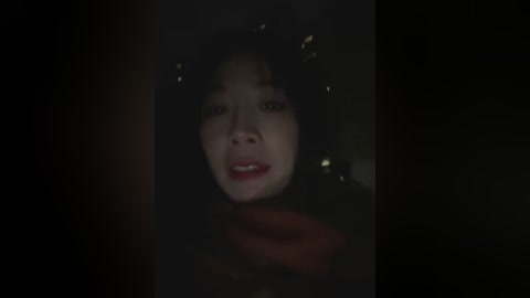 Video of a distressed, middle-aged woman with curly black hair and pale skin, wearing dark clothing, crying and looking up with a pained expression. Background is dark and blurry, creating a dramatic, intense atmosphere.