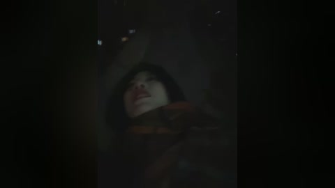 A dimly lit video shows a person with fair skin and dark hair, eyes closed, and mouth open, possibly in pain or distress. The background is dark and blurry, suggesting a nighttime setting.