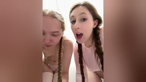 Video of two young women, one with braids, leaning over a penis, both looking surprised.