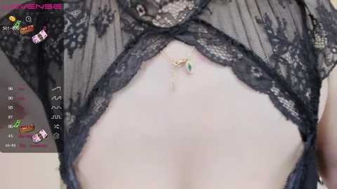 A close-up video of a woman's bare midriff, wearing a sheer black lace lingerie top with intricate floral patterns. A small, delicate green gem is prominently placed on her navel, adding a touch of sparkle.