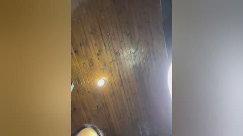 A video showing a close-up of a wooden ceiling with a circular light fixture, featuring a warm, golden-yellow light source. The ceiling appears weathered with visible grain patterns and a slightly worn texture.