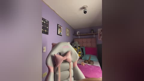 A video of a child's bedroom with light purple walls, a grey chair, a pink bed, stuffed animals, and a mounted camera.