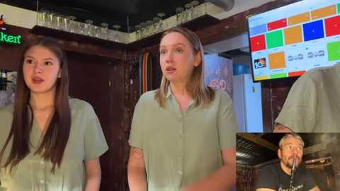 Video of three women in green shirts on a stage, with a colorful digital screen behind them and a man singing.