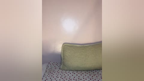 A video of a bed with a beige pillow and white polka-dot duvet cover in a dimly lit room, with a soft light source creating a diffused glow on the walls.