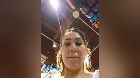 Video of a young woman with wet hair, wearing a white shirt, playing air guitar with exaggerated facial expression. Background shows a dimly lit room with colorful lights and a blurred, chaotic scene.