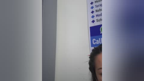 Video of a partially obscured person with dark hair, seen through a frosted glass door, with a blue schedule poster partially visible.