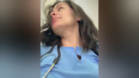 A video of a woman in a blue hospital gown, with long brown hair, leaning back in a chair, eyes closed, and an IV drip attached.