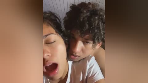 Video of two young men with curly hair, one in a white shirt, kissing passionately, blurred background.