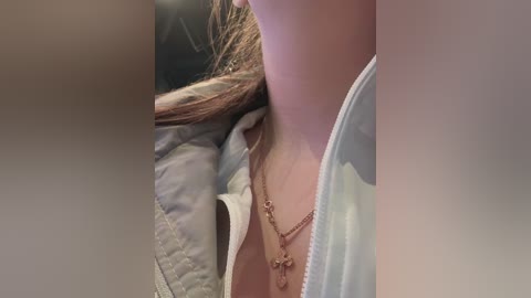 Video of a close-up of a woman's neck and chest, wearing a white shirt and a gold necklace, with a blurred background.