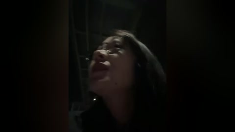 A dimly lit video shows a woman with long dark hair, eyes closed, mouth open, possibly in distress or ecstasy, against a dark, blurred background.