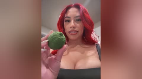 A video of a curvaceous woman with long red hair, wearing a black top, holding a green broccoli in her right hand. The background is blurred.