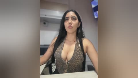Video of a Latina woman with long black hair, wearing a low-cut, leopard print top, sitting at a desk in an office setting.