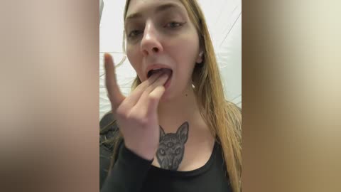 Video of a young Caucasian woman with long blonde hair, wearing a black shirt, licking her finger while showcasing a large wolf tattoo on her chest.