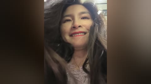 A video of a smiling woman with long, dark hair, wearing a lace top, seen from the waist up, slightly out of focus.