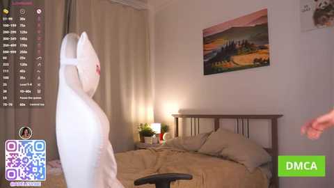 Video of a modern bedroom with a white cat-shaped plush toy, beige bedspread, potted plant, and framed landscape painting on the wall.