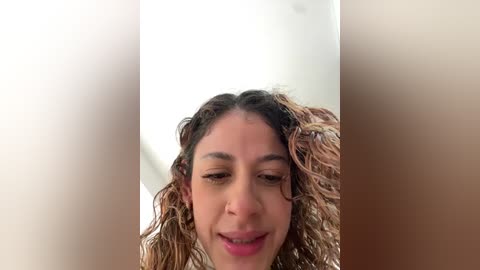 Video of a young woman with curly, shoulder-length hair, light brown skin, and a smile, set against a blurred, white background.