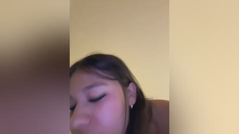 A blurry video of a young woman with light brown skin and long, straight dark hair, eyes closed, lying on a beige surface.