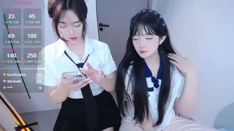 A video of two Asian women, one in a white blouse and black skirt, the other in a blue sailor outfit, seated side by side, both appearing distressed, with a digital thermometer overlay displaying temperatures.