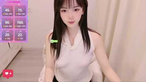 Video of a young Asian woman with long black hair, wearing a white sleeveless dress, seated indoors, with a virtual dating app overlay showing her stats.