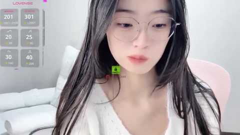 Video of a young Asian woman with long black hair, wearing large glasses and a white shirt, seated indoors with a virtual reality headset.