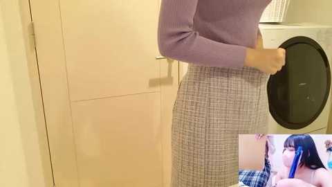 Video of a person in a purple sweater and checkered skirt standing next to a white washing machine. Inset: close-up of a woman in a blue plaid shirt kissing a man.