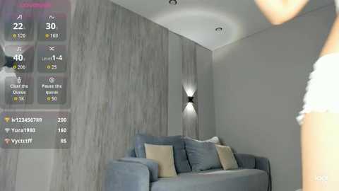 Video of a modern living room with a grey couch, beige cushions, textured grey wall, and a minimalist black wall sconce.