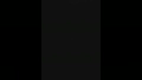 A dimly lit, black-and-white video features a vertical strip of light in the center, surrounded by complete darkness, creating a stark contrast. The image is minimalist, emphasizing the stark division between light and shadow.