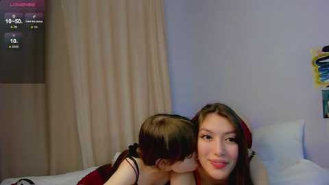 Video of a young woman with long brown hair and a young girl with short brown hair, both in casual clothes, kissing on a bed in a dimly lit room.